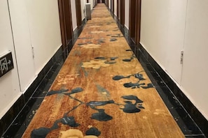 Ein Hotelgang mit einem gemusterten Teppich, schwarzem Marmorboden und weißen Wänden.