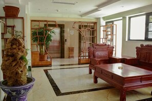 A traditional-style room with a wooden sofa, a dining table, and a potted plant. - Hedu Hotel (Zhaotong)