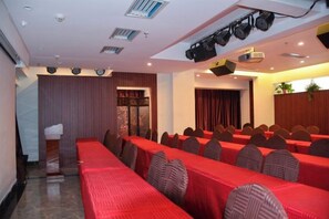 Un salón de conferencias con filas de mesas, sillas y un escenario con un proyector.
