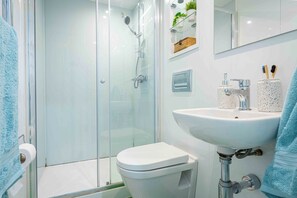 Un baño moderno con cabina de ducha de vidrio, un lavamanos blanco y un inodoro.