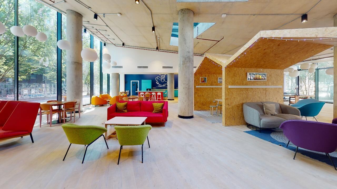 A spacious indoor area with large windows, a wooden structure, and colorful seating arrangements.