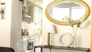 Une cuisine moderne dotée d’appareils électroménagers en acier inoxydable, d’un miroir rond avec un cadre doré et d’un vase rempli de fleurs posé sur une console.