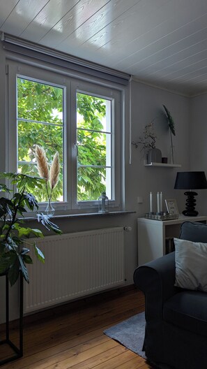 A room with a large window, radiator, and a dark-colored sofa.