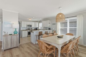 A modern kitchen with white cabinets, a central island, and a dining area with wicker chairs.