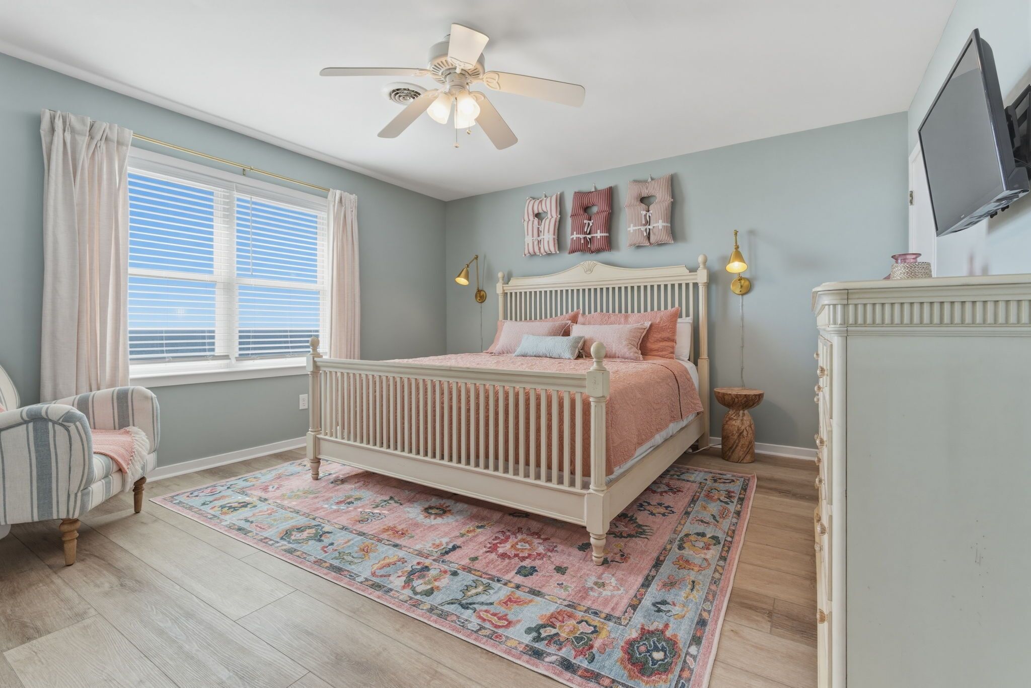 A bedroom with a bed, a chair, a ceiling fan, a window with curtains, and wall decorations.