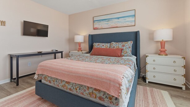 A bedroom with a bed, bedside tables, a desk, a TV, and a painting on the wall.