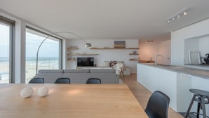 A modern living space with a dining area, kitchen, and a large window overlooking the beach. - Apartment Knokke-heist With Sea View (Knokke-Heist)