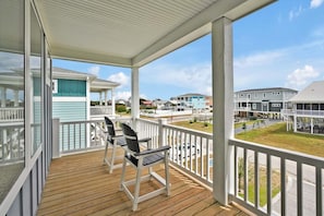 A covered balcony with wooden flooring, white railings, and two chairs.