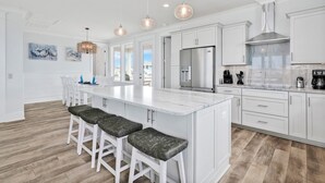 A modern kitchen with white cabinetry, a large island with bar stools, stainless steel appliances, and pendant lighting.