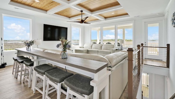 A spacious kitchen with a large island, bar stools, a ceiling fan, and a view of the outdoors.
