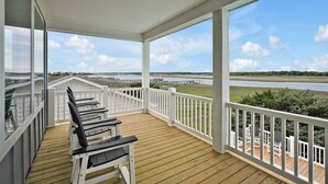 A covered deck with wooden flooring and white railings, overlooking a river and distant landscape.