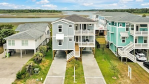 A coastal residential area with multi-story houses featuring balconies, a central walkway, and a view of the water.