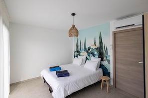 Quarto com cama, luminária na parede, porta e um mural.