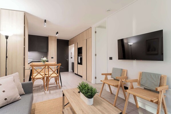 En moderne stue med sofa, træstole, spisebord og et fjernsyn ophængt på væggen.
