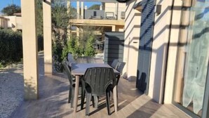 An outdoor patio area with a table and chairs, a pergola structure, and a view of neighboring buildings. - 70m2 house with large terrace in secure residence with swimming pool. (Bonifacio)