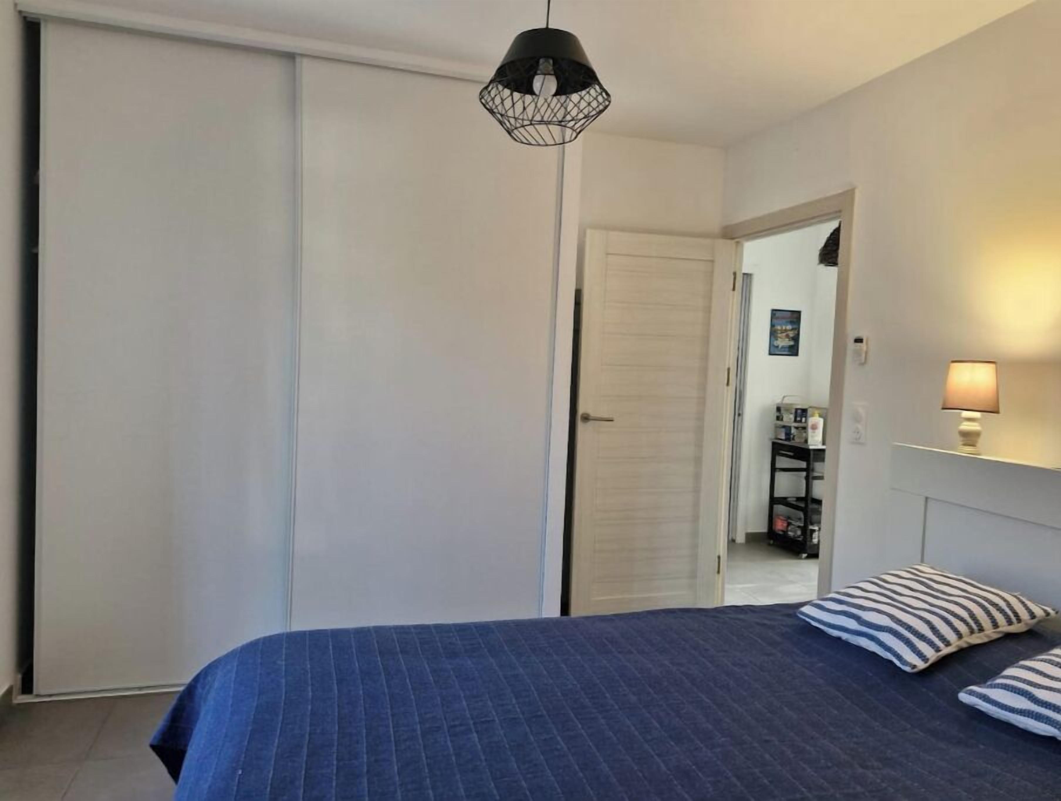 Un dormitorio con una cama grande, un armario, una lámpara colgante y una mesita de noche con lámpara.