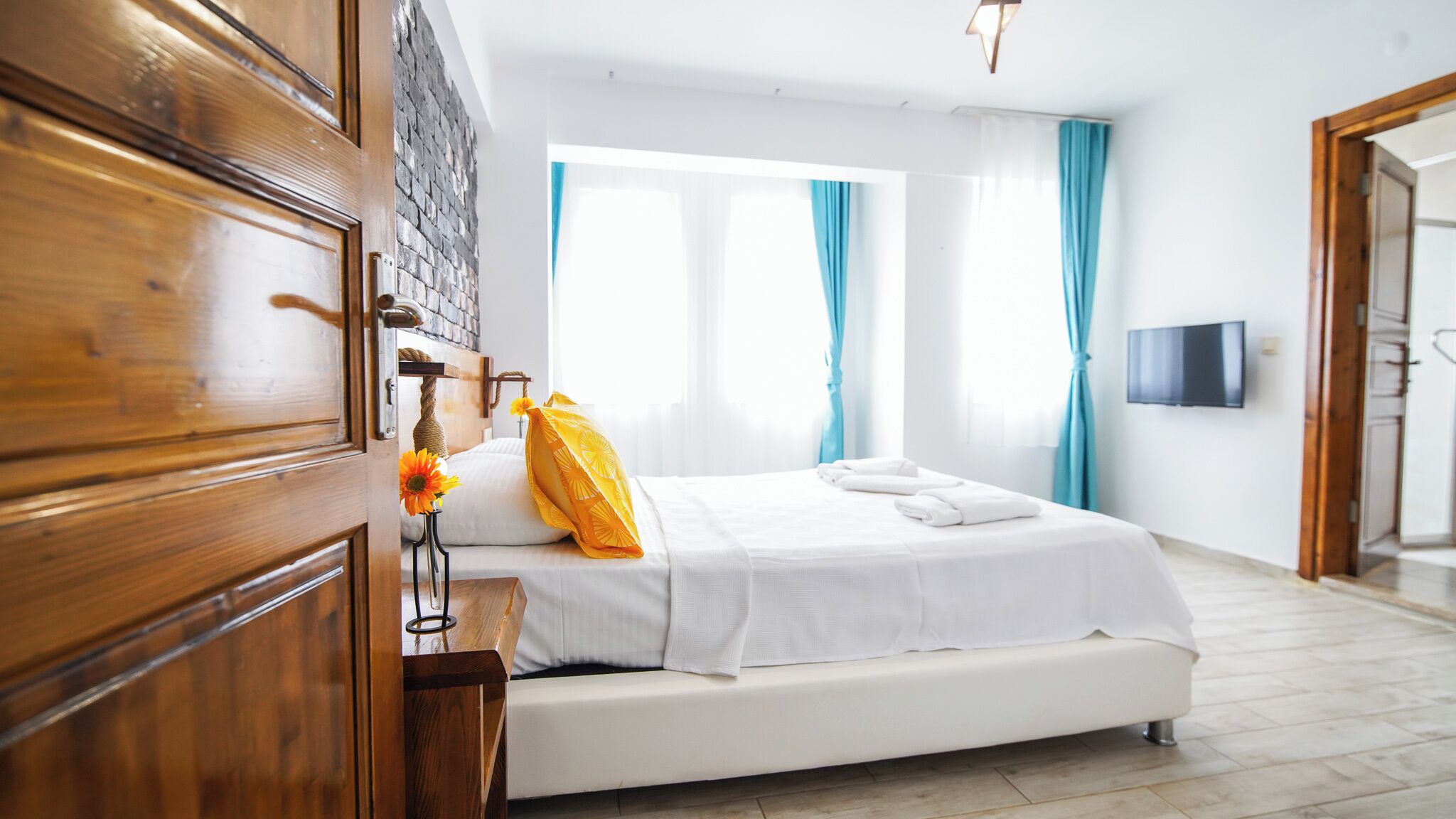 A hotel room with a bed, wooden wardrobe, a TV mounted on the wall, and a window with curtains.
