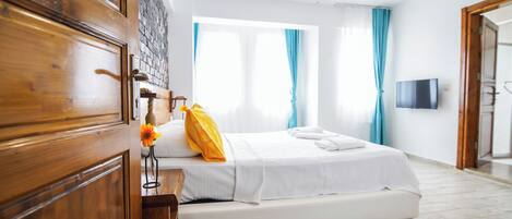 A hotel room with a bed, wooden wardrobe, a TV mounted on the wall, and a window with curtains.