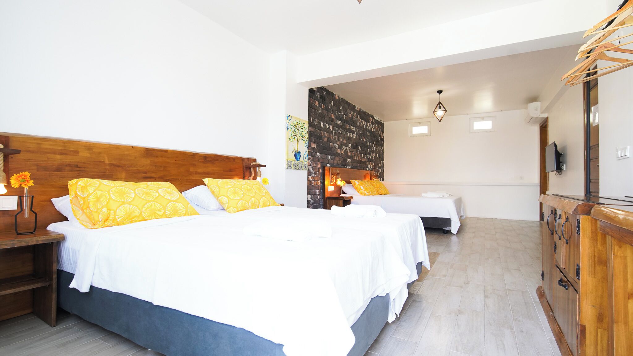 A hotel room with two beds, wooden headboards, a brick accent wall, a wooden cabinet, and a small painting.