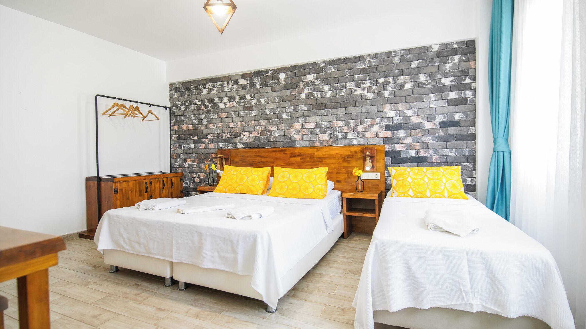 A hotel room with two beds, a brick-patterned wall, wooden headboards, and a wooden nightstand with a lamp.