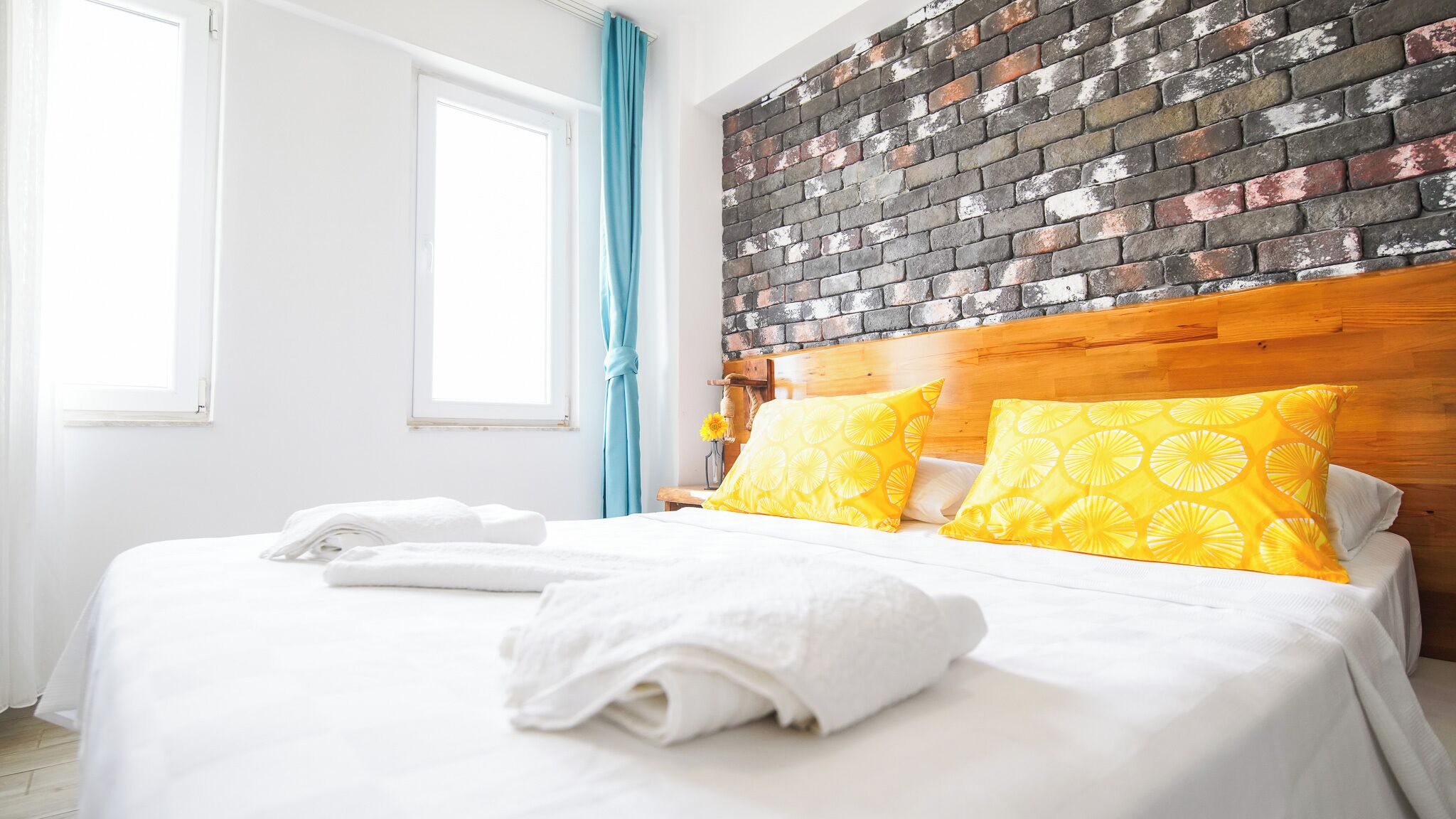 A hotel room with a brick-patterned headboard, white bedding, and a window with blue curtains.