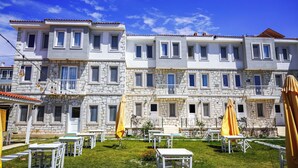 A multi-story building with stone facade, balconies, and outdoor seating areas with umbrellas.