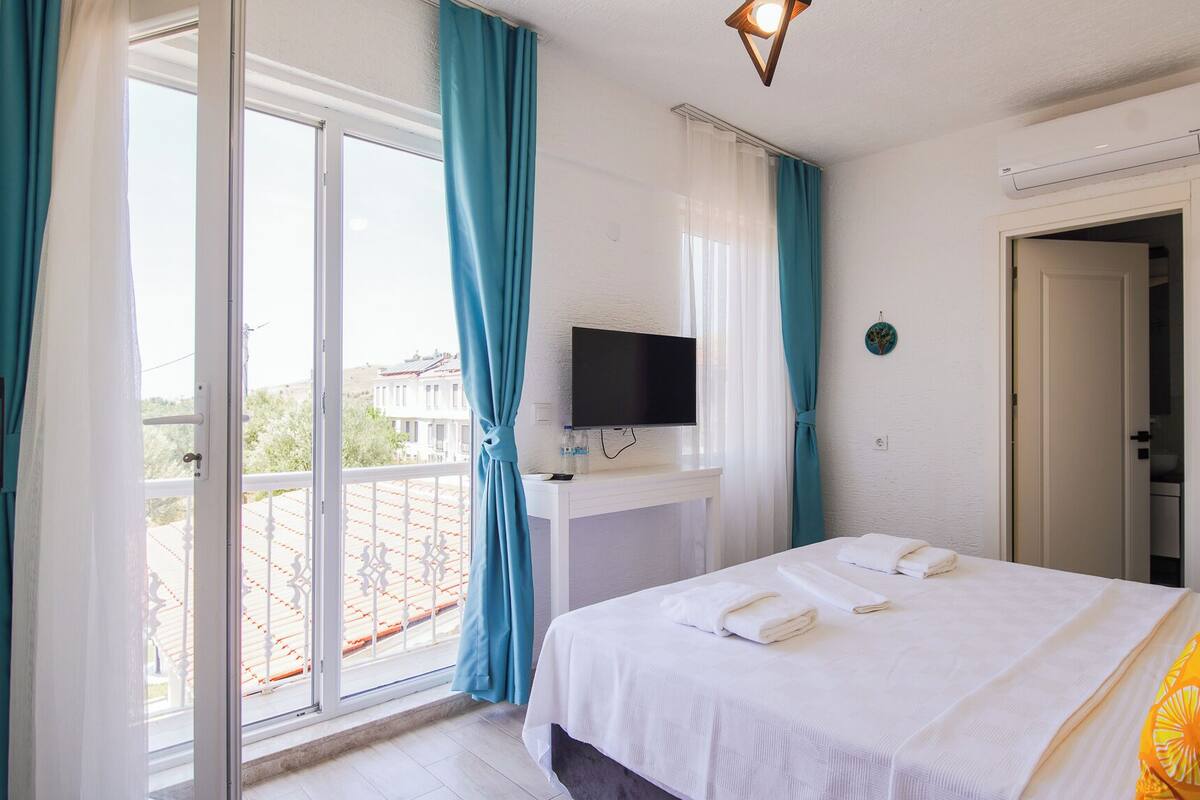 Habitación de hotel con cama, televisión, balcón con barandilla y una puerta.