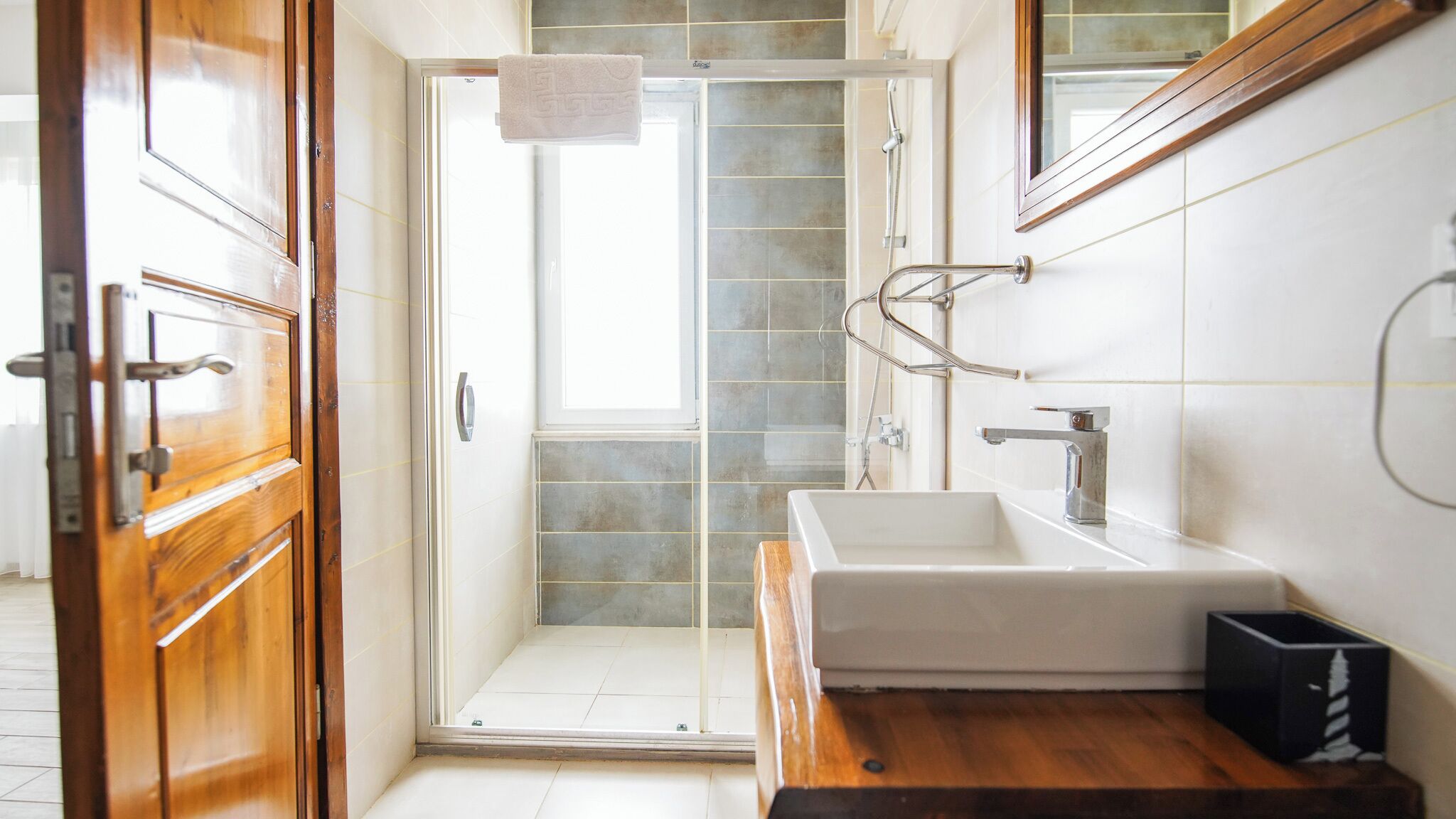A modern bathroom with a glass shower door, a white sink, and a wooden vanity.