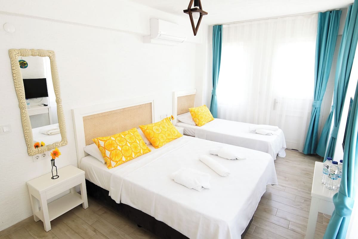Una habitación de hotel con dos camas, un espejo grande, una mesita y un televisor.