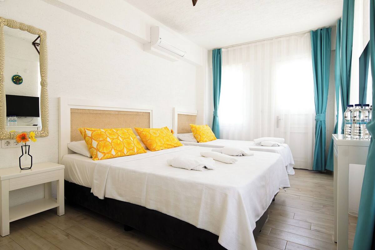 Habitación de hotel con dos camas, un espejo grande, una mesita de noche con un jarrón de flores y una ventana con cortinas.