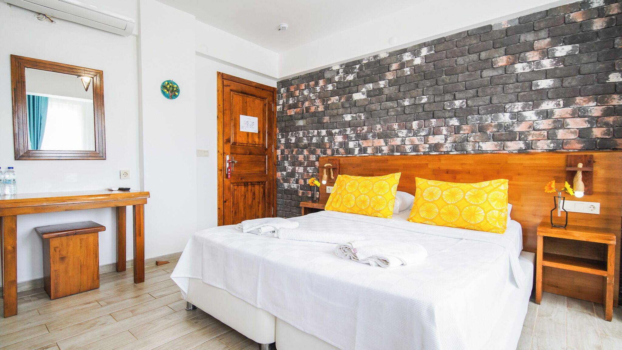 A hotel room with a bed, wooden nightstands, a desk, and a mirror.