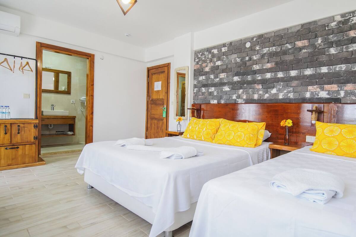 Habitación de hotel con dos camas, cabeceros de madera, una pared decorativa de ladrillo y un armario de madera.