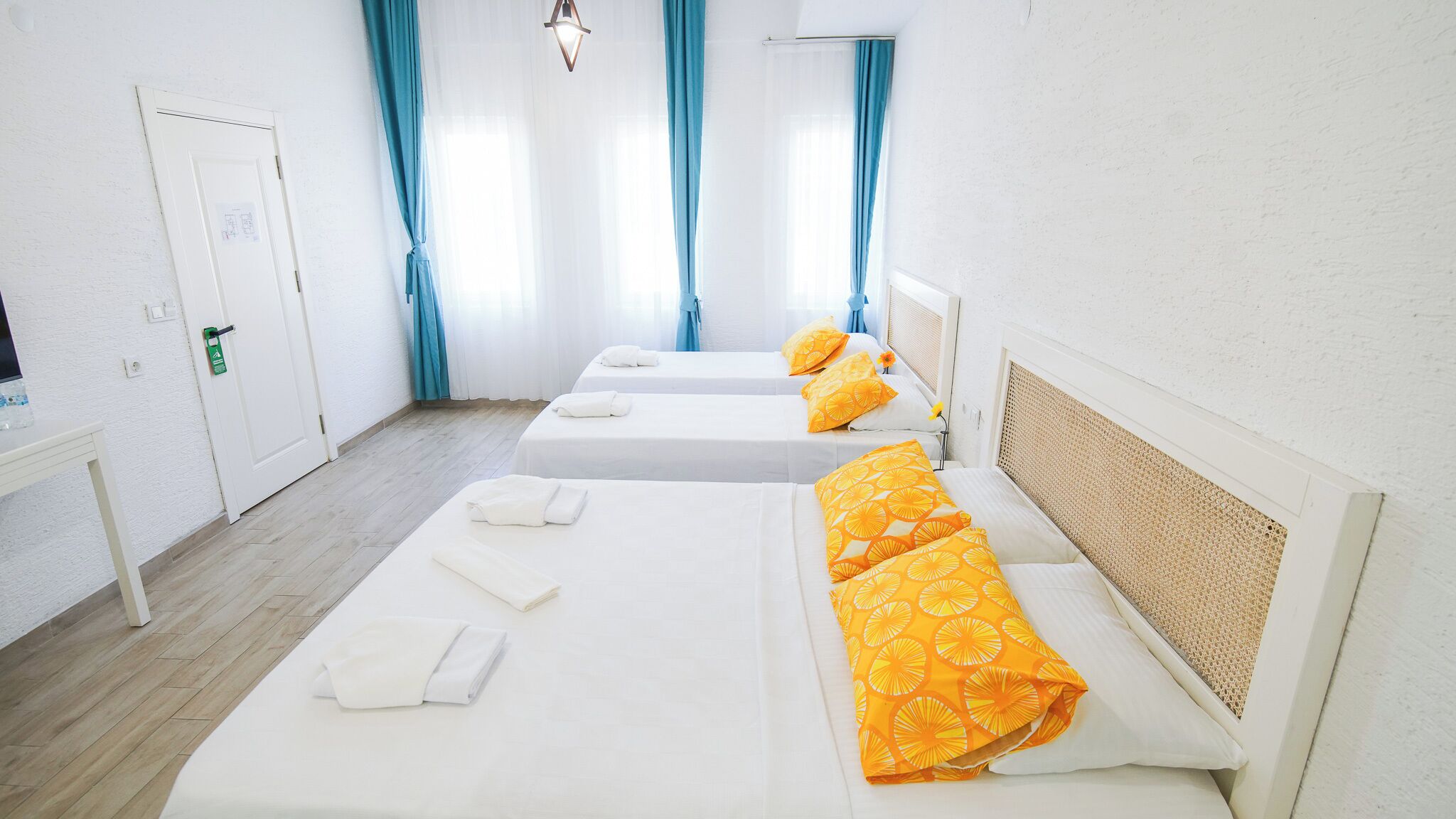 A hotel room with three beds, each with white linens and orange pillows. There is a small table with a bottle of water and a green sign.