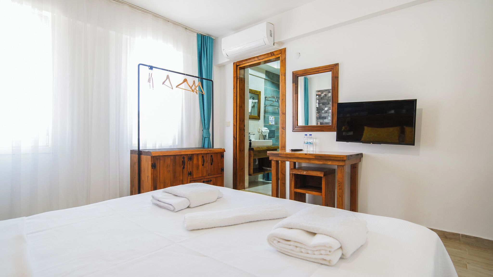 A hotel room with a bed, a wooden dresser, a mirror, a television, and a window with curtains.