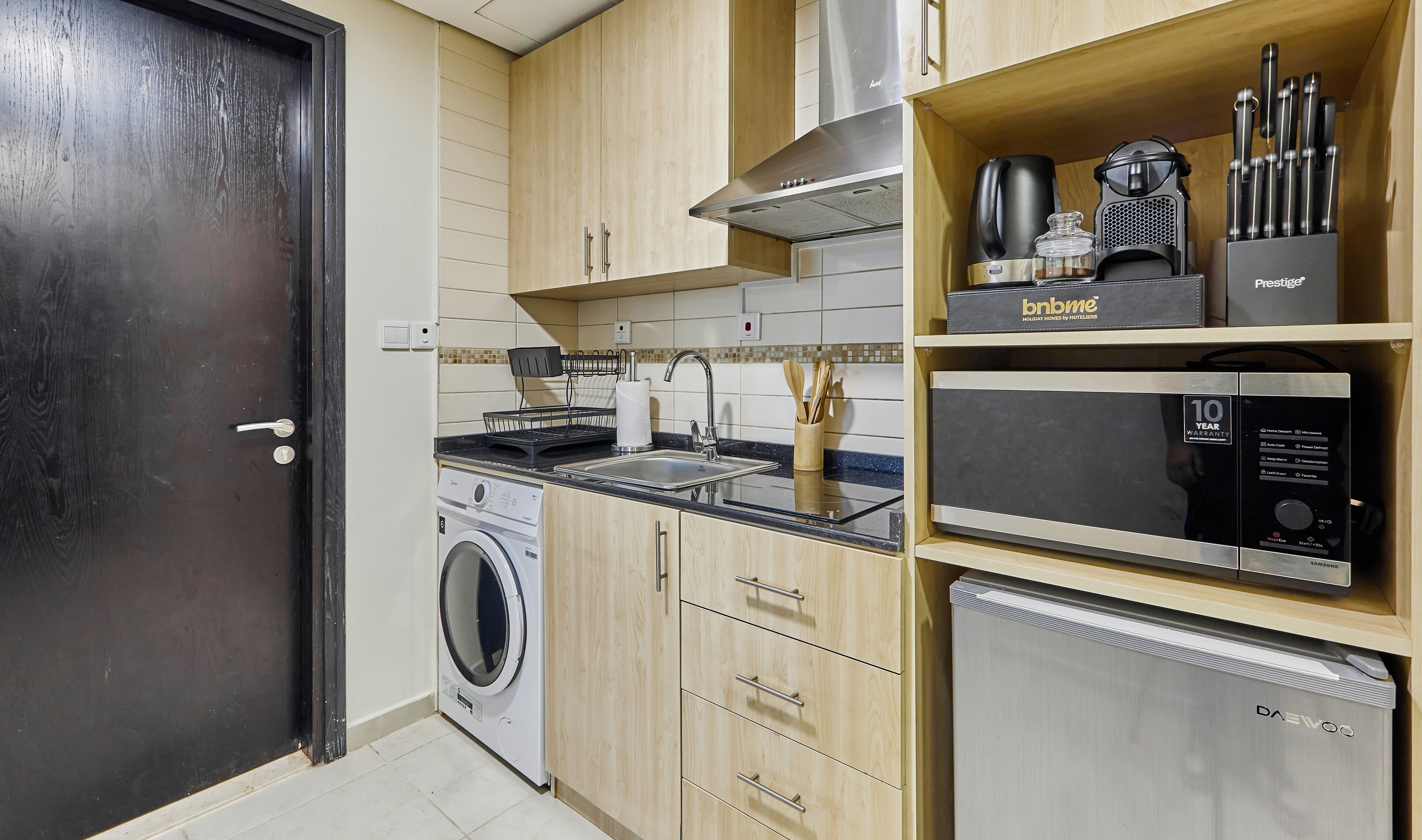 A compact kitchen with a washing machine, a microwave, and a coffee maker on the countertop.