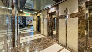 A modern elevator area with marble flooring and glass walls, featuring emergency exit signs and service elevators. - bnbme - Gold Crest Views 2 - STUDIO (Dubai)