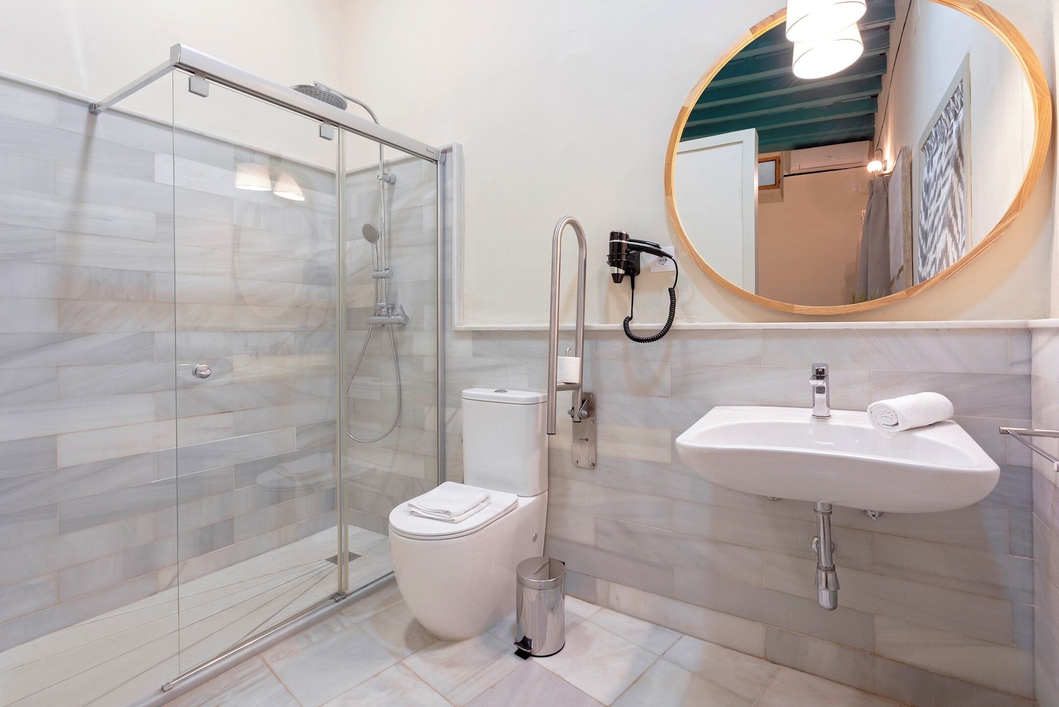 A modern bathroom with a glass-enclosed shower, a white toilet, a sink with a towel, and a mirror with a wooden frame.