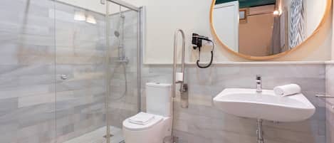 A modern bathroom with a glass-enclosed shower, a white toilet, a sink with a towel, and a mirror with a wooden frame.