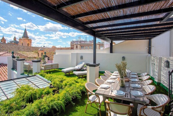 A rooftop terrace with a dining table set for six, surrounded by wicker chairs, a pergola, and a view of historic buildings. - Sevillian House With Terrace. Augusto Plasencia (Seville)