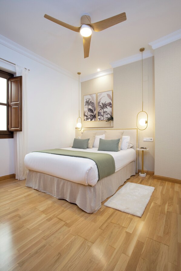 A neatly arranged bedroom with a bed, a ceiling fan, a bedside table with a lamp, and a wall-mounted artwork. - Charming 1bedroom Apt. in Granada. San Agustín (Granada)