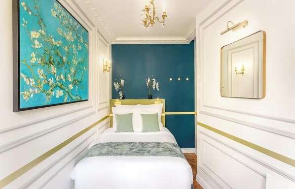 A bedroom with a bed, a large painting, a mirror, and a chandelier.