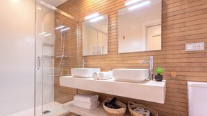 Un baño moderno con cabina de ducha de vidrio, dos lavamanos, un espejo y paneles de madera en las paredes.