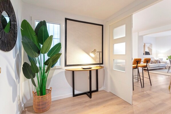 A modern living room with a large potted plant, a round table with a lamp, and a white sofa with two chairs.