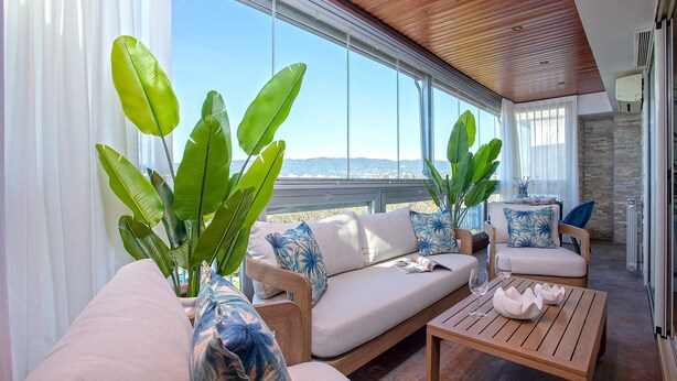 A modern outdoor seating area with a sofa, chairs, and a wooden table, surrounded by large green plants and a view of the landscape. - Bright Stay Córdoba. Paseo de la Victoria (Córdoba)