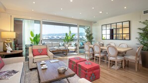 A spacious living room with a large window, a dining area with wooden furniture, and a cozy seating area with a sofa and ottomans. - Bright Stay Córdoba. Paseo de la Victoria (Córdoba)