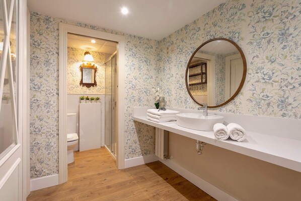 Un baño con papel tapiz floral, un lavabo blanco, un espejo y un inodoro.