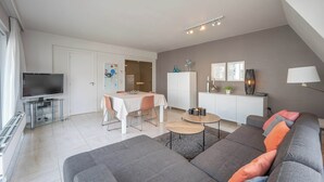 A modern living room with a gray sofa, a dining table, and a TV. - Knokke Beach Hideaway (Knokke-Heist)