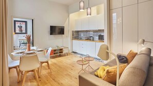A modern living room with a sofa, a dining table with chairs, and a kitchen area with cabinets and a TV. - Superb Apartement Center of Paris Le Marais (Paris)