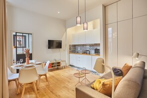 Een moderne woonkamer met een bank, een eettafel voor vier personen en een keuken met witte kasten en een betegelde spatwand.