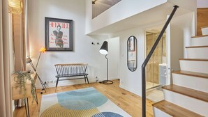 A modern interior with a staircase, a framed magazine on the wall, a bench, and a floor lamp. - Superb Apartement Center of Paris Le Marais (Paris)